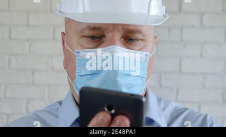 Engineer with Safety Helmet and Medical Face Mask Talking to Mobile Stock Photo