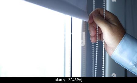 Image with the Hand of a Man Inside a Hotel Room, Bedroom or Office, Opening a Vertical Curtain on the Window Stock Photo