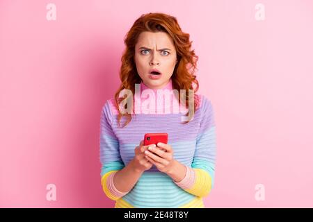 Photo portrait of offended woman with open mouth holding phone with two hands isolated on pastel pink colored background Stock Photo