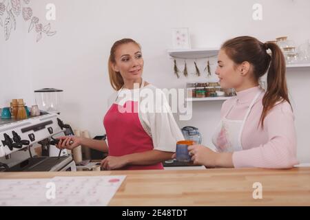 Attractive female barista talking to her coworker while preparing coffee on a coffee machine at the cafe Stock Photo