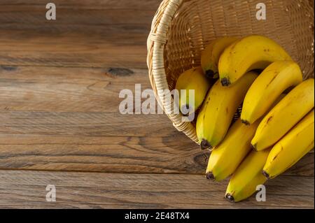 Rip bunch of bananas in wicker basket on wooden background. Healthy eating concept. Stock Photo