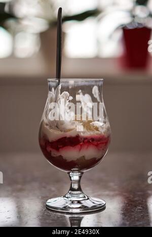 Vertical shot of a delicious half-empty dessert cup with a spoon on a reflective surface Stock Photo