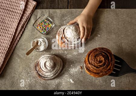 Children's hand takes a freshly baked cinnamon bun. Stock Photo
