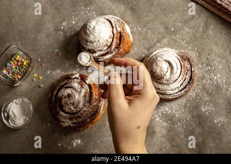 Woman's hand sprinkles icing sugar on fresh baked cinnamon buns. Stock Photo