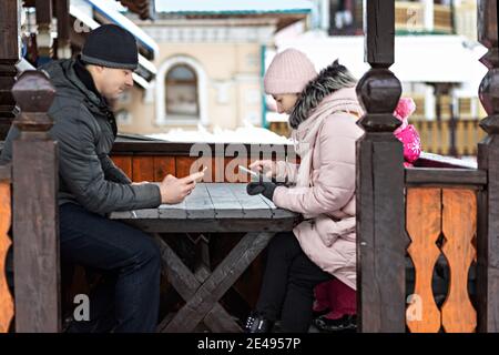 A couple is waiting for their order for lunch in a street cafe, texting by phone. Communication with people on a smartphone Stock Photo