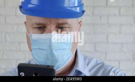 Engineer with Safety Helmet and a Protection Mask on His Face Text Using Cell Phone Stock Photo