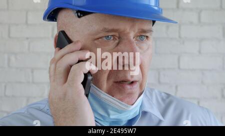 Engineer with Safety Helmet and a Protection Mask on His Face Talking to the Cell Phone Stock Photo