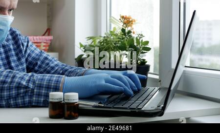 Sick Man with Protective Gloves in Hands Using a Laptop. Social Distancing Lifestyle in Pandemic Period Stock Photo