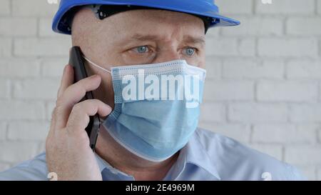 Engineer with Safety Helmet and a Protection Mask on His Face Talking to the Cell Phone Stock Photo