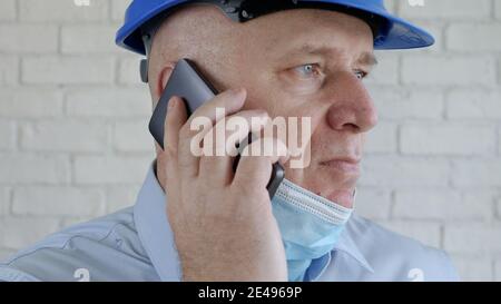 Engineer with Safety Helmet and a Protection Mask on His Face Talking to the Cell Phone Stock Photo