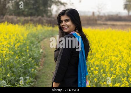 a pretty Indian woman with smiling face looking back in mustard field with hair all over face Stock Photo