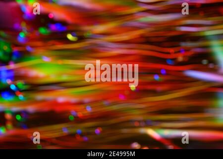 Defocused dots and horizontal tendrils of color in red, green, blue, and yellow created by LED lights photographed outdoors at night. Stock Photo