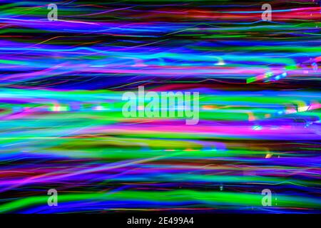 Defocused horizontal movement of green, blue, yellow, and pink created by LED lights photographed outdoors at night. Stock Photo