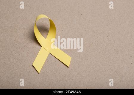 Yellow awareness ribbon on cardboard background. Stock Photo