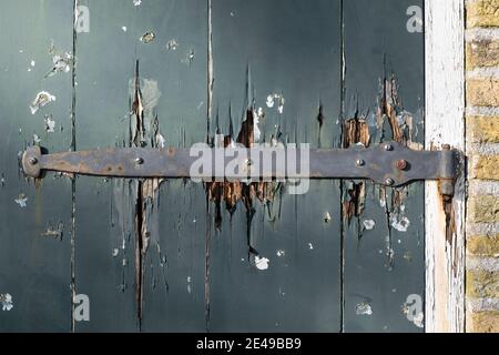 Long antique metal hinge on an old door with chipped paint in a white frame next to a wall of typical Dutch yellow bricks Stock Photo