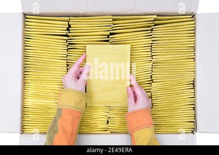 Female hands hold one bubble envelope over an open box full of padded post mailers. Top view, isolated on white. Stock Photo