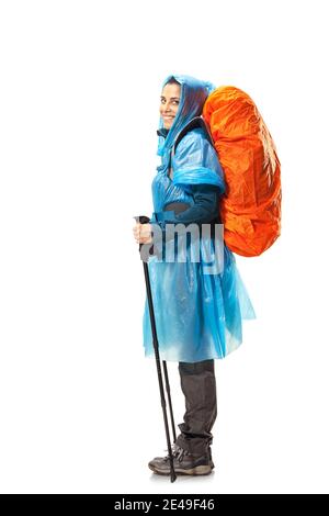 girl with hiking equipment and large backpack, wearing blue raincoat, posing in studio isolated on white. Stock Photo