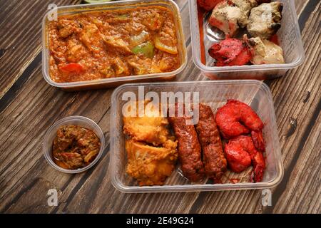 Top view of traditional Indian food in a plastic box on a wooden table. Indian fast food delivery at home. Stock Photo