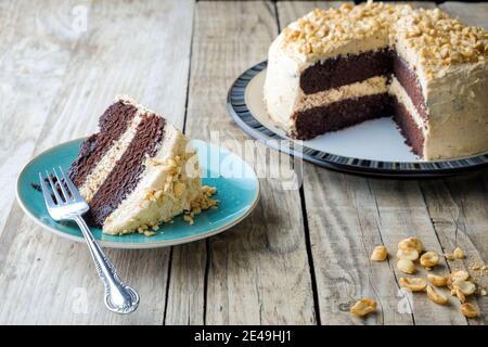 A freshly baked, peanut butter and chocolate cake. The cake has a thick buttercream filling and top and a slice is served on a side plate plate Stock Photo