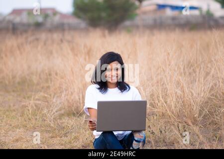 pretty young black woman smiling while using her laptop and credit card outdoor in a park Stock Photo