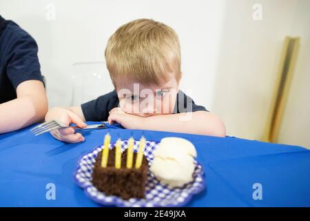 Child Sits at Table Staring at birthday Candles in Piece of Cake Stock Photo