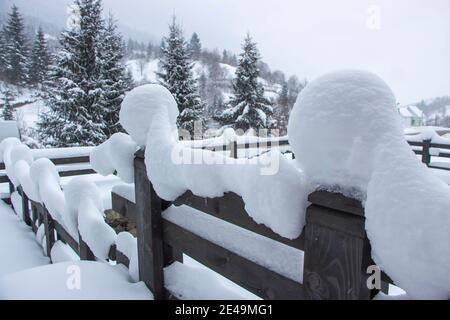 Snow on a wooden fence near the house in the mountains between Christmas trees and spruces. Selective focus Stock Photo