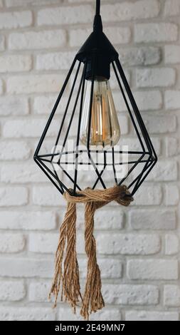 Loft lamp in the interior, a lamp against a brick wall, a pendant lamp decorated with a rope. Stock Photo