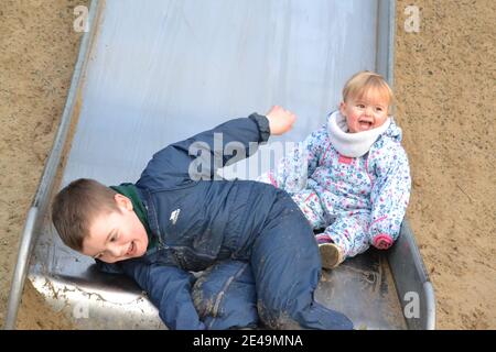 Fun At The Park - On The Slide -  Siblings Playing - Brother And Sister - Laughing And Smiling - UK Stock Photo