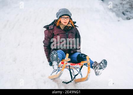 Young Woman is riding seldge at mountain track in winter having fun, Oberaudorf, Hocheck, German Alps, Europe, Stock Photo