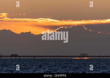 Southend Pier at sunrise, with fiery sky above and a glimpse of the sun on the horizon under the pier. Rough Thames Estuary. Out towards North Sea Stock Photo