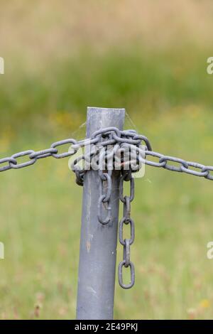 Industrial chain attached to a galvanised fence post in a green field Stock Photo