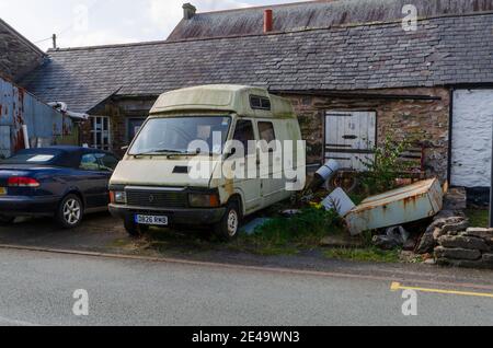 Bala; UK: Sep 20, 2020: A n old rusting abandoned camper van or mobile home is parked outside a low roof, stone building. Stock Photo