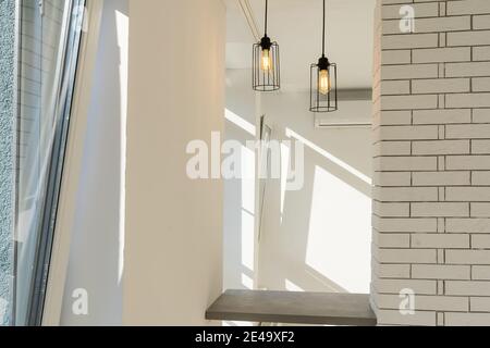 Two steel lamps illuminate a bar table against a wall in a modern minimalist style with a white color on the wall above the counter and brown below Stock Photo