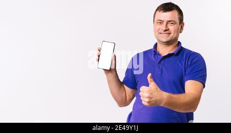 Banner. Deaf senior man shows thumb up while holding a mobile phone, white screen to the camera. White background and blank advertising space. Stock Photo