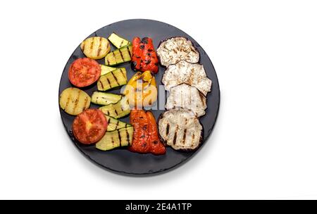 grilled vegetables on round black stone plate isolated on white background. top view, flat lay,copy space Stock Photo