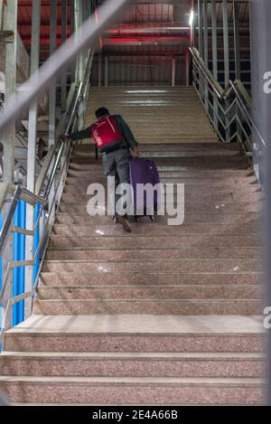 Man climbing stairs with heavy luggage at Vasai Road Railway Station, Maharashtra, India Stock Photo