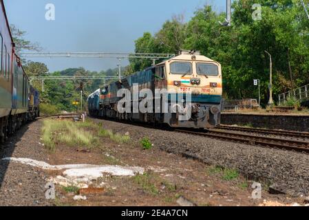 Freight train crossing 02413 Madgaon - Delhi Hazrat Nizamuddin Rajdhani Special at beautiful scenic Pernem Railway Station on Konkan Railway. Stock Photo