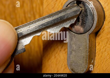 A hand puts the key in the keyhole. The key inserted in a wooden door lock, close up view. Stock Photo