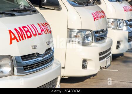 Front part of ambulances standing in parking lot of hospital. A row cars of rescuers with red text ambulance on hood. Stock Photo