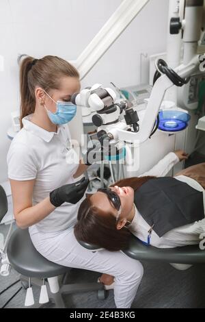 Professional dentist wearing medical face mask, using dental microscope on patient Stock Photo