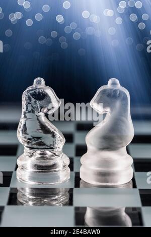 Glass chess pieces on a glass chessboard with reflection, on a blue background. Stock Photo