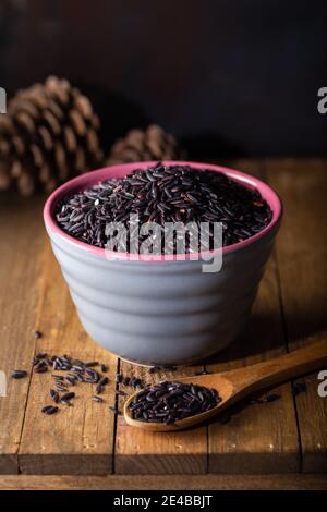 Black wild rice in ceramic bowl on wooden background. Thai black jasmine rice (Rice berry). Stock Photo