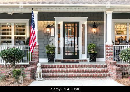 Front door entrance to a large two story blue gray house with wood and vinyl siding and a large American flag. Stock Photo