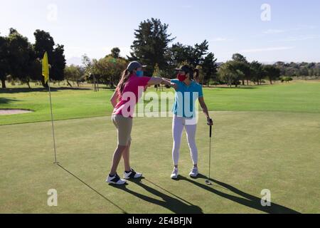 Two caucasian women wearing face masks playing golf bumping elbows Stock Photo