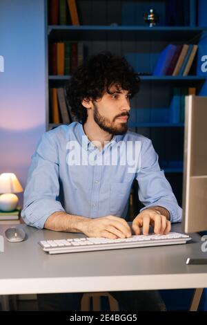 Close-up face of focused bearded man looking intently at monitor screen while working on computer. Stock Photo