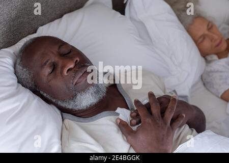 Senior mixed race couple in bedroom lying on bed sleeping. staying at home in self isolation during quarantine lockdown. Stock Photo