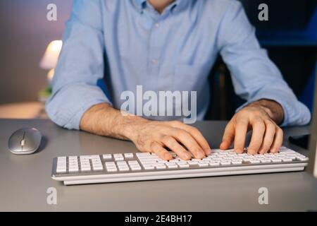 Close-up of hands of unrecognizable man using wireless keyboard and computer mouse at dark room. Stock Photo