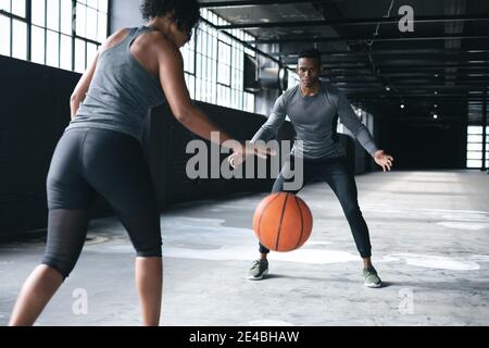 African american man and woman standing in an empty urban building and playing basketball Stock Photo