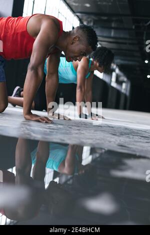 African american man and woman wearing sports clothes doing push ups in empty urban building
