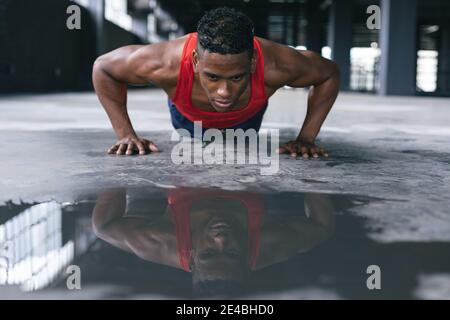 African american man wearing sports clothes doing push ups in empty urban building